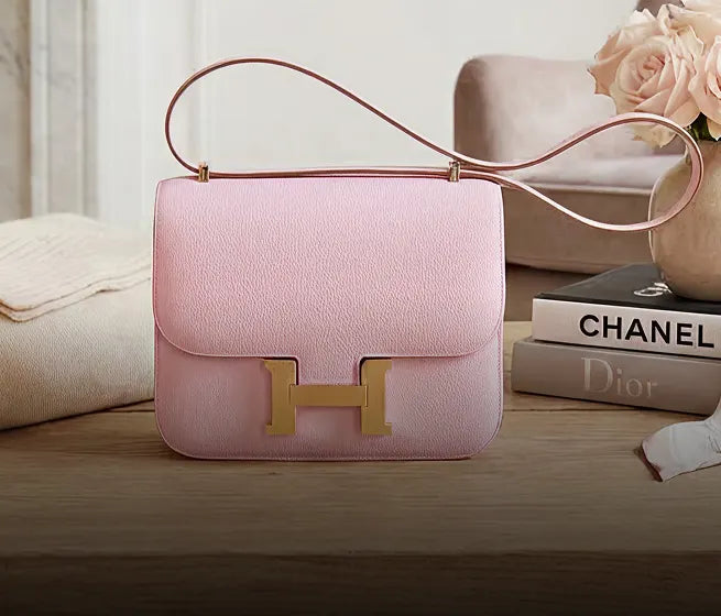 A pink Hermés bag with books in a wood table.
