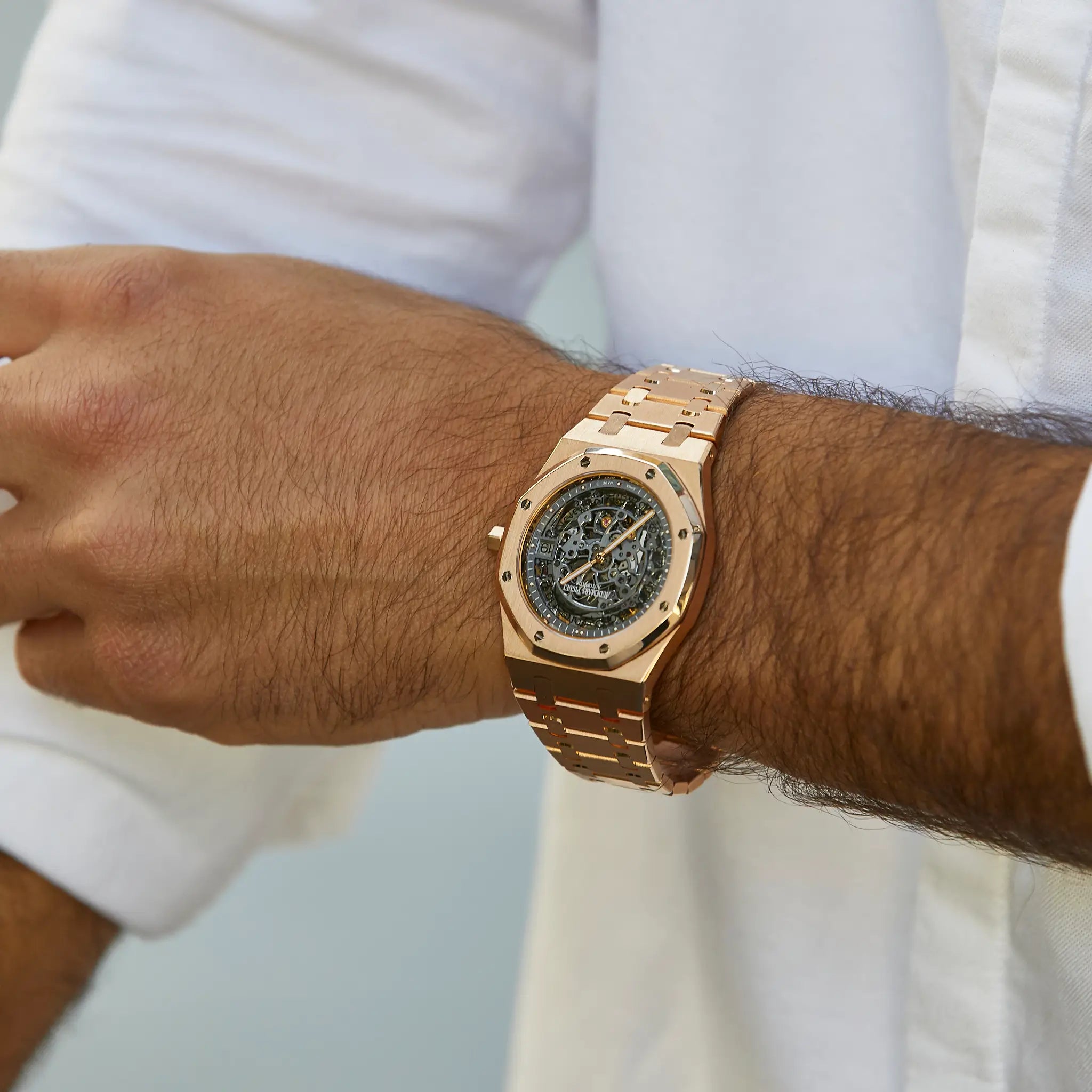 Rose gold skeleton watch on wrist with white shirt