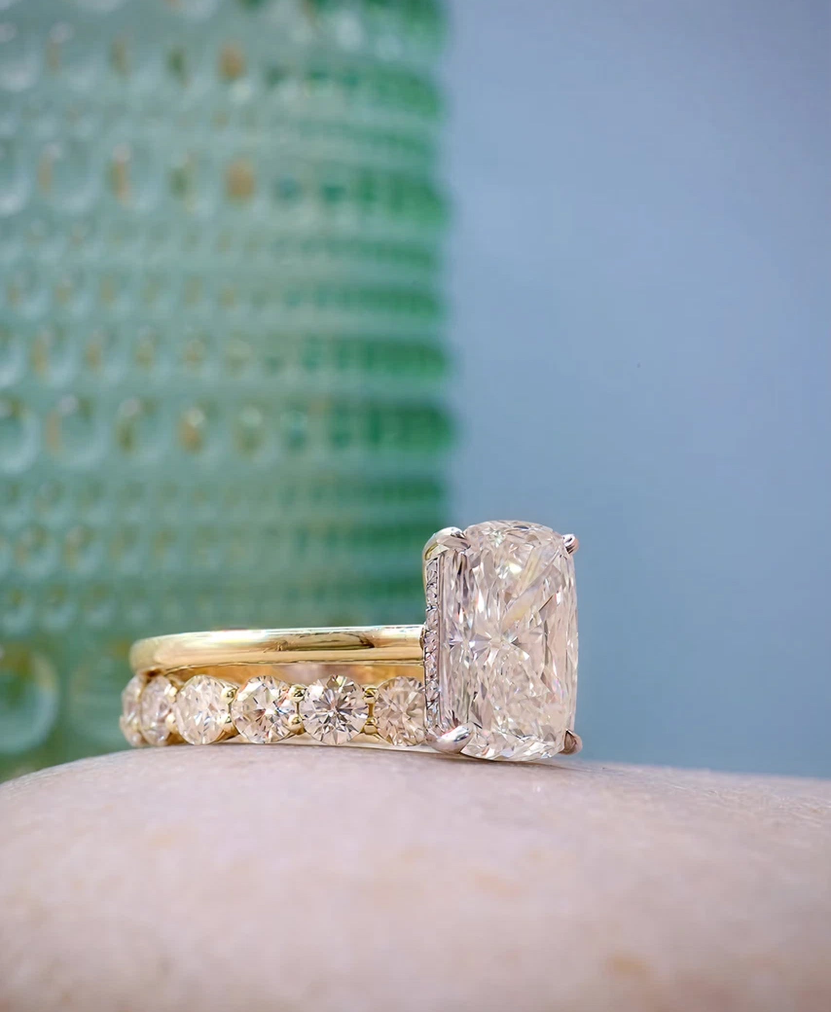 Gold ring with a large diamond and smaller diamonds on a marble surface with a green and blue gradient background.
