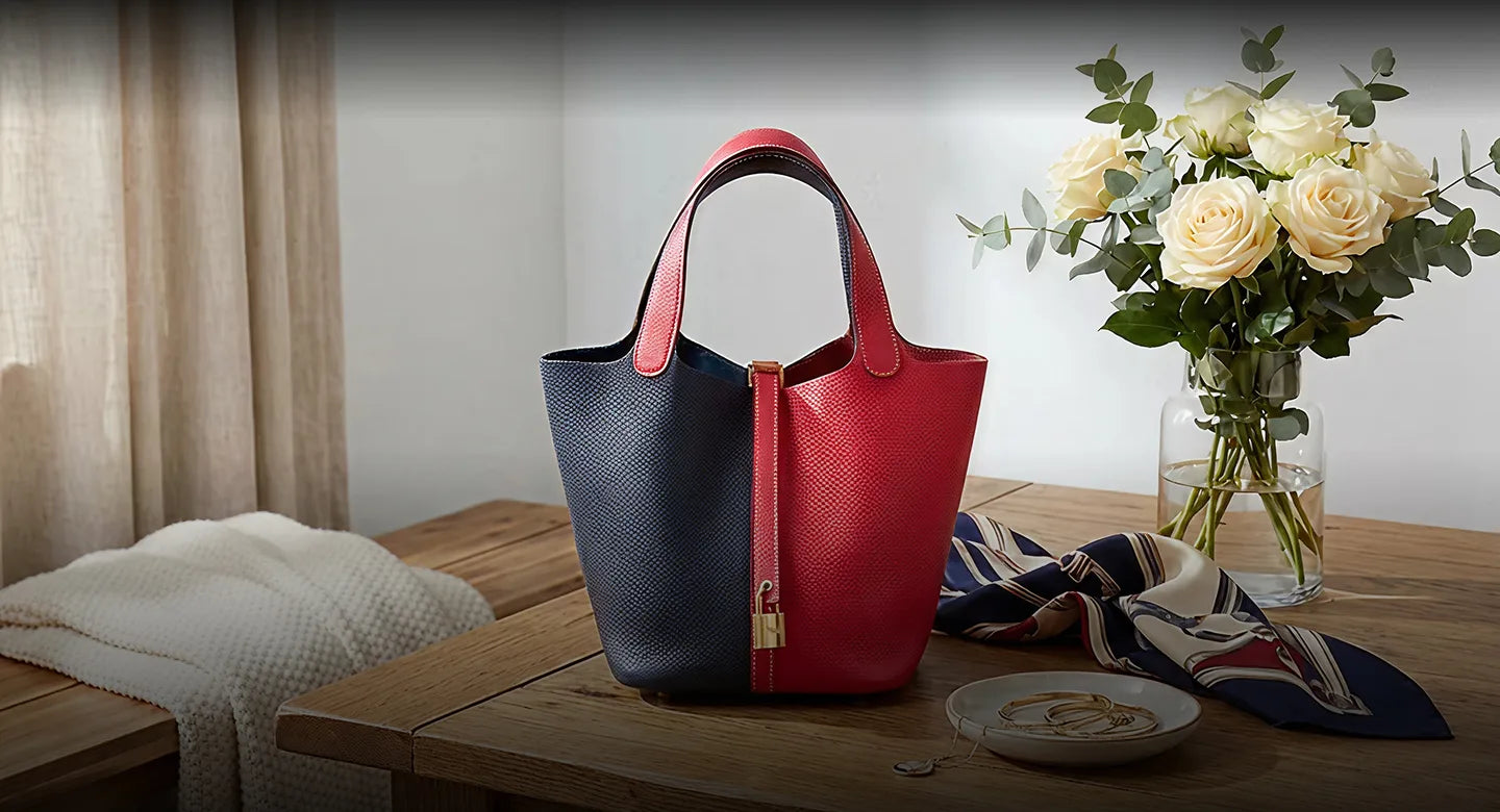 Two-toned red and blue handbag on a wooden table with flowers and a blanket.