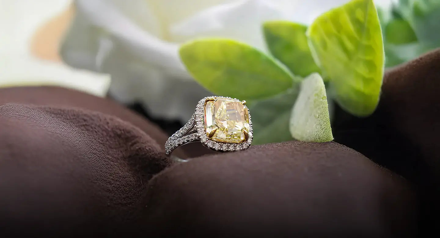 Gold ring with a large diamond on a brown surface with green leaves in the background