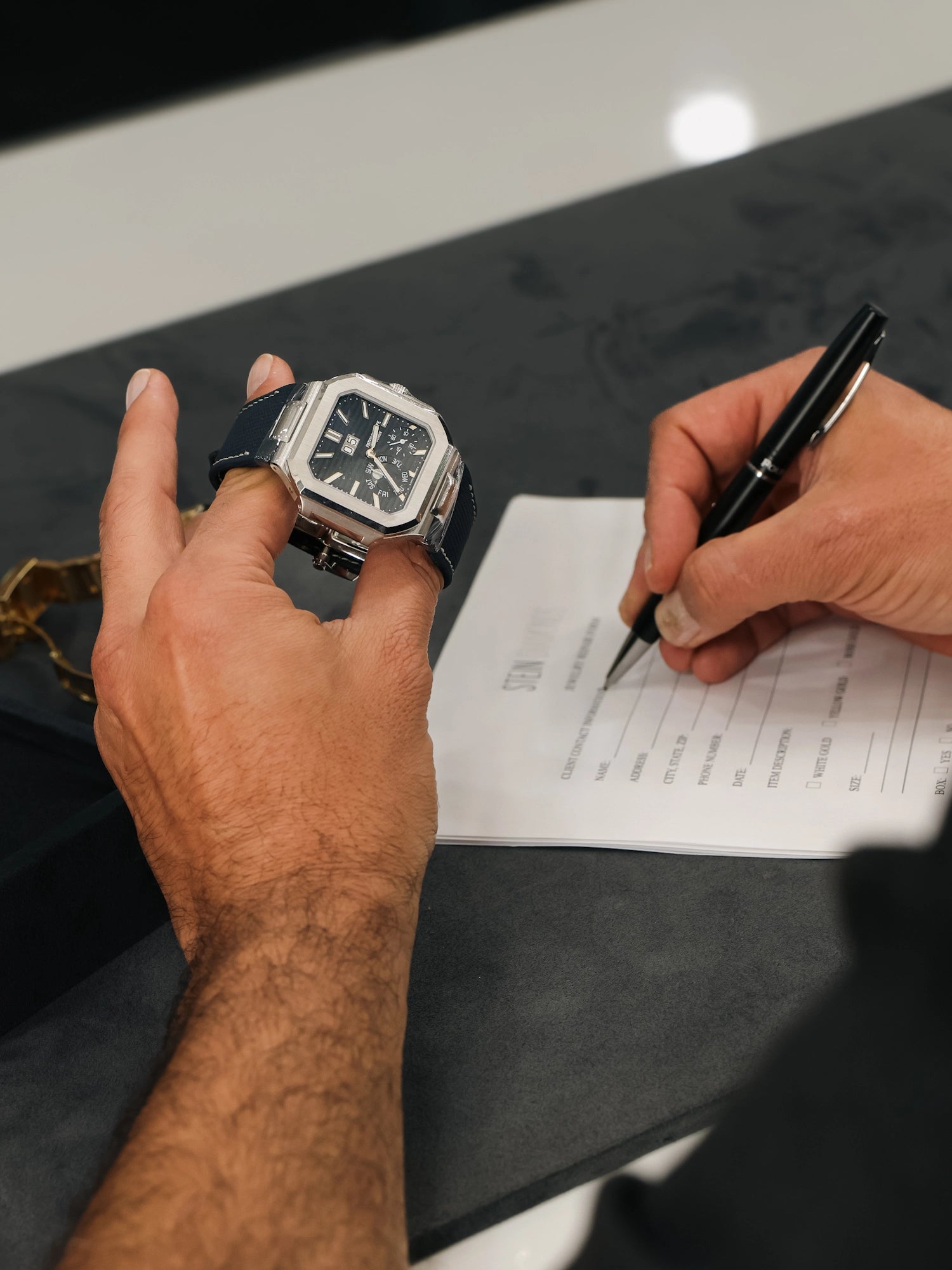 Person holding a luxury watch and writing on a document with a pen.