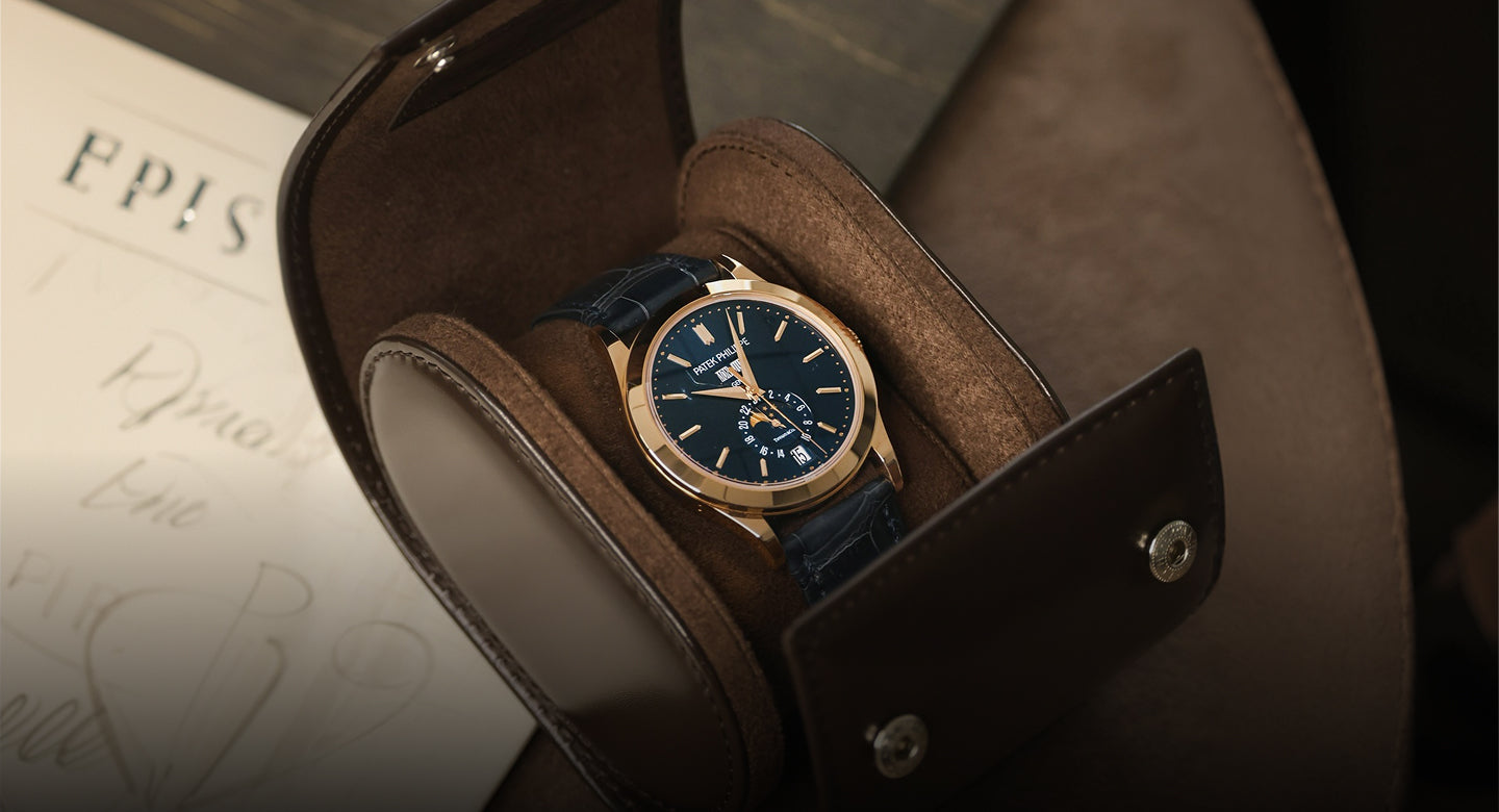 Luxury watch with blue face and gold accents in a brown leather box on a textured surface.