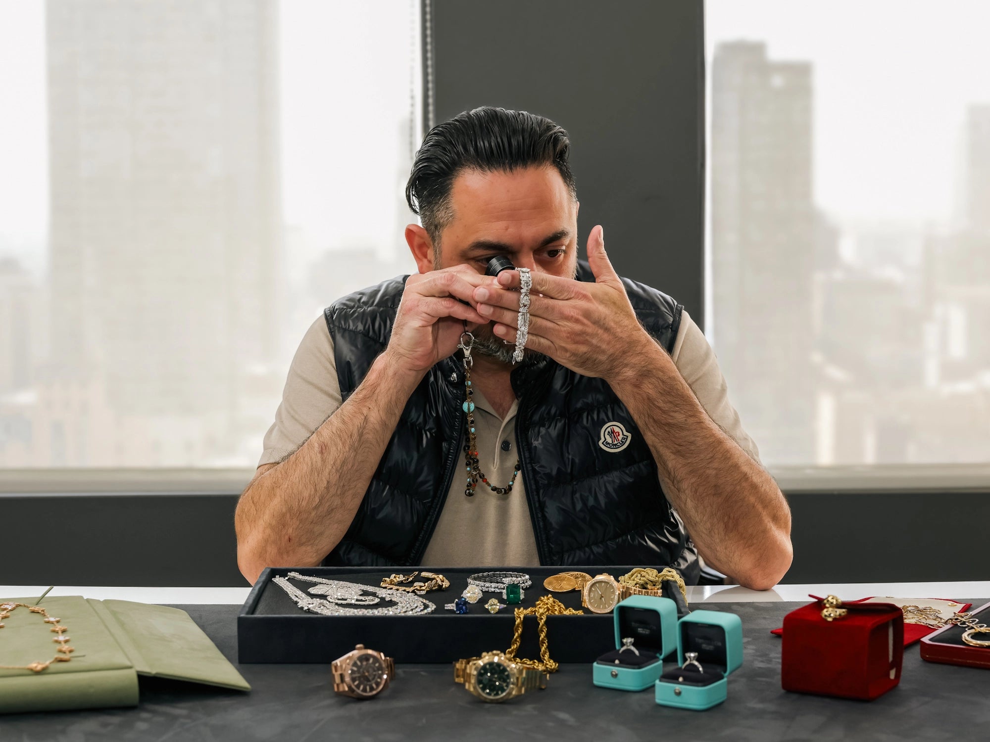 Man examining jewelry on a table with a cityscape background